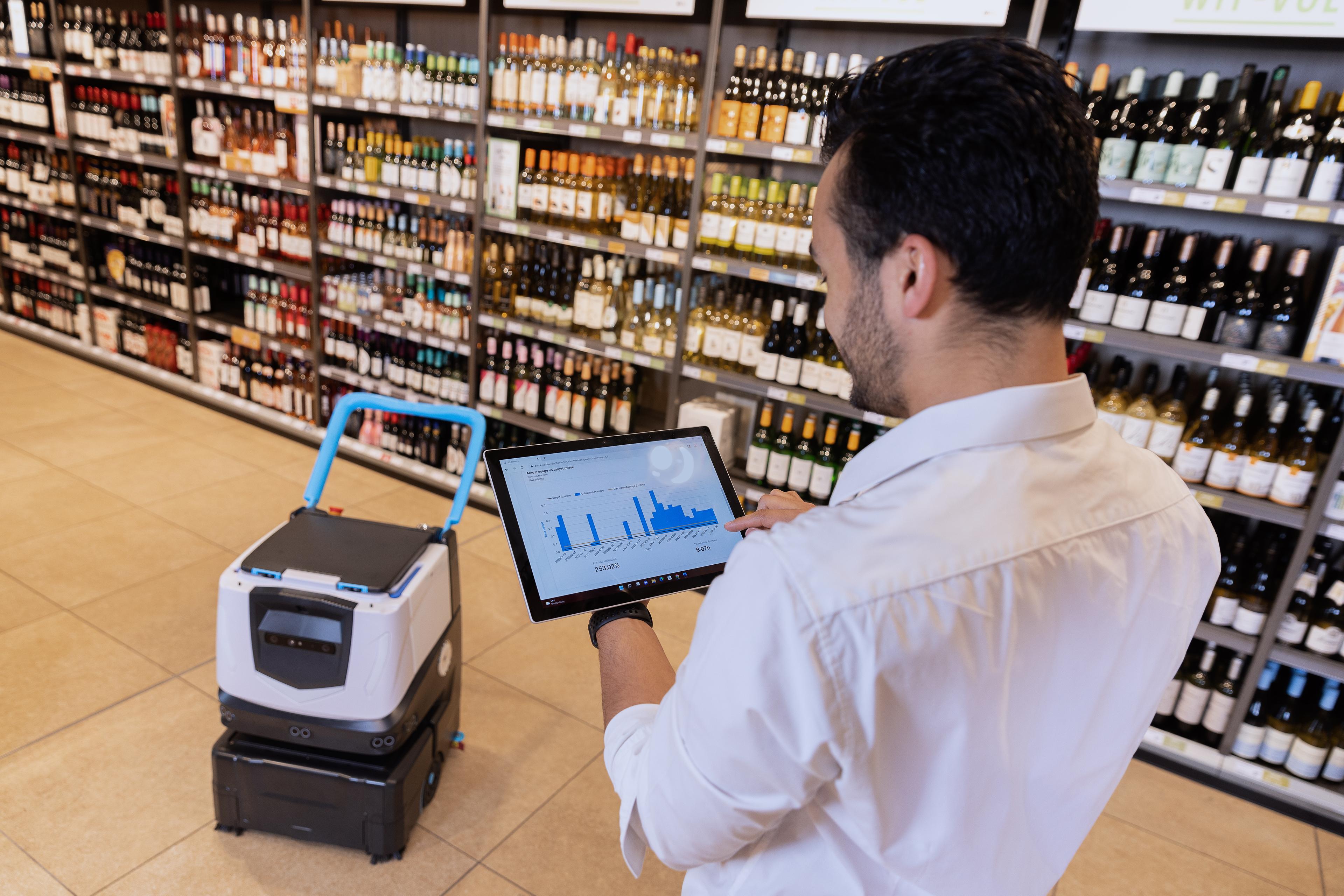 person reviewing Isynergy fleet mangement on ipad while Cobi 18 robotic floor scrubber cleans retail store